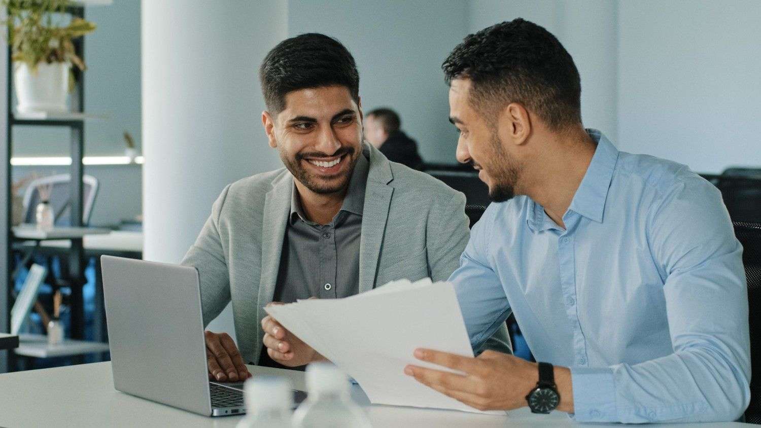 two successful arab male businessmen sitting office holding paper documents diverse smiling young scaled